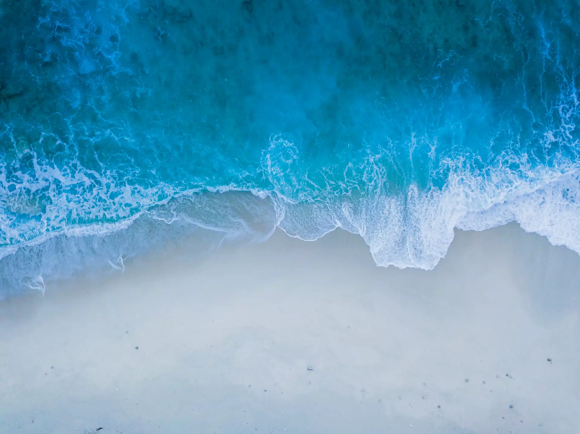 Aerial view of ocean waves reaching sandy beach