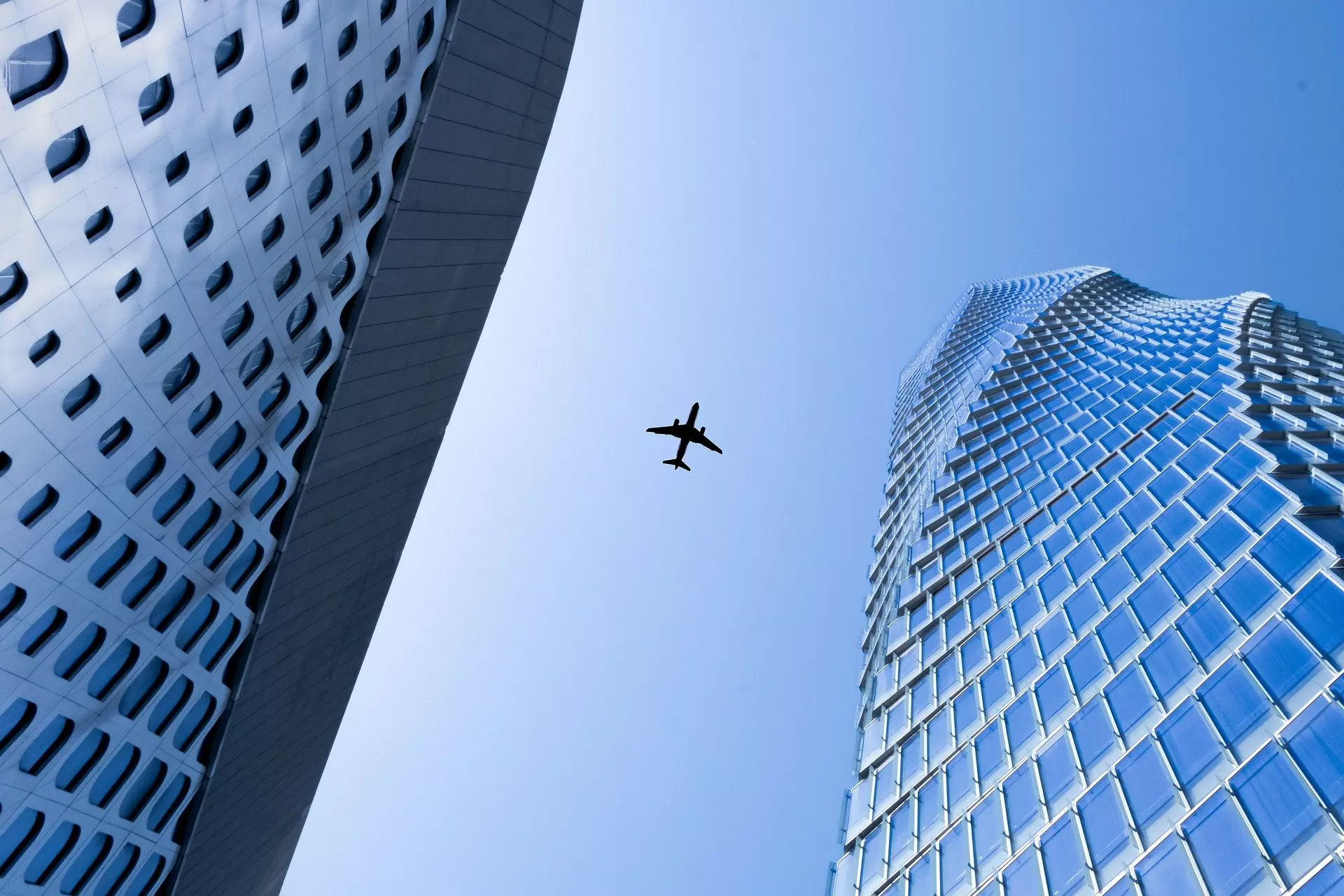 Skyscrapers viewed from below with a plane silhouetted against a blue sky