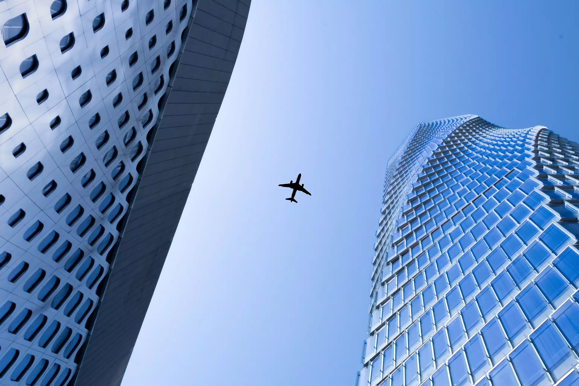Skyscrapers viewed from below with aircraft silhouetted against blue sky