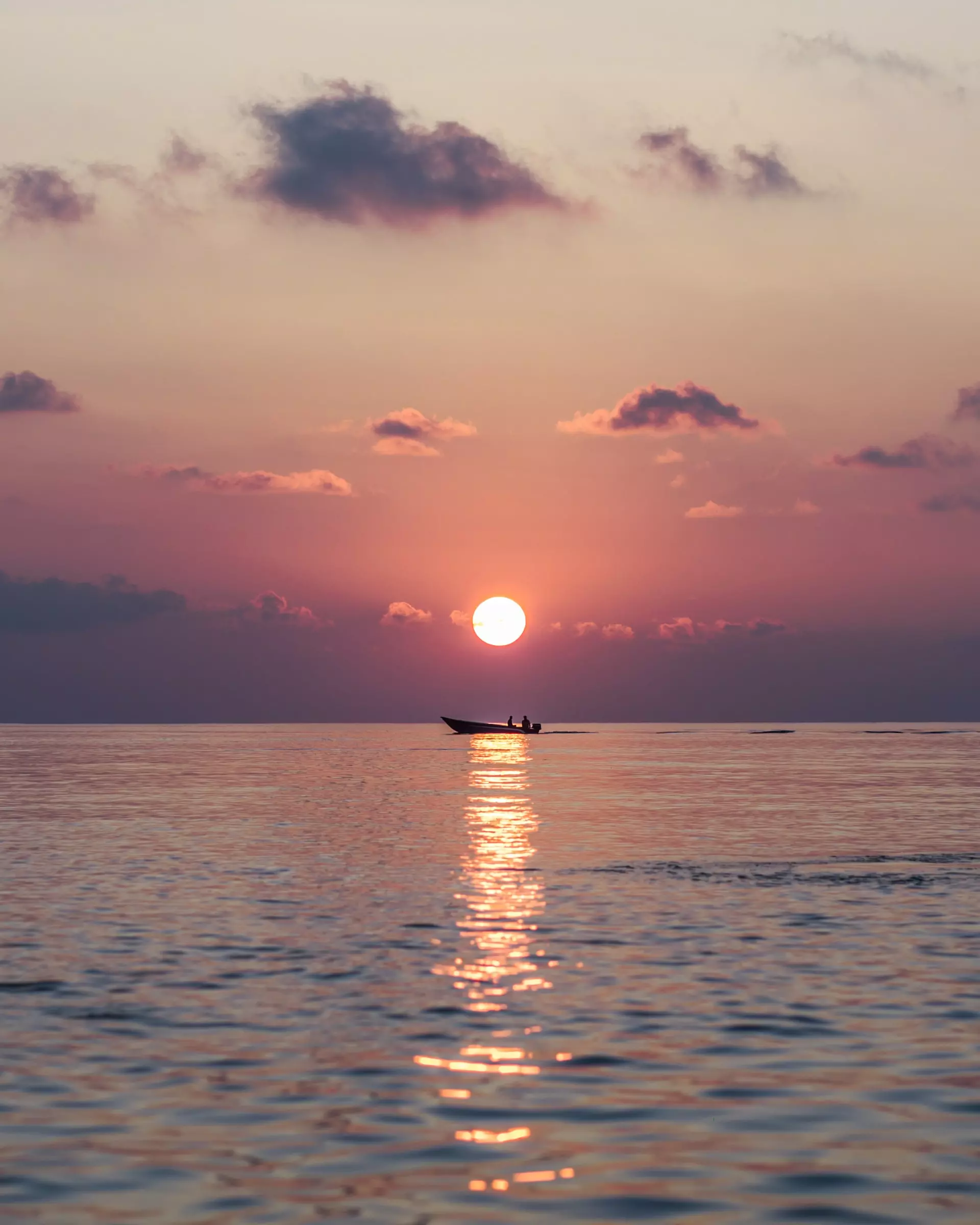 Sun setting over a small boat on a calm sea