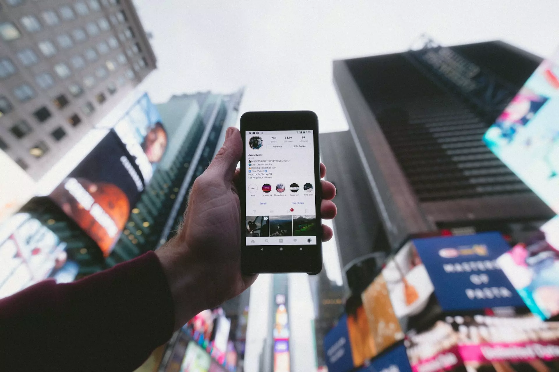 A hand holding a mobile phone up against a backdrop of city streets