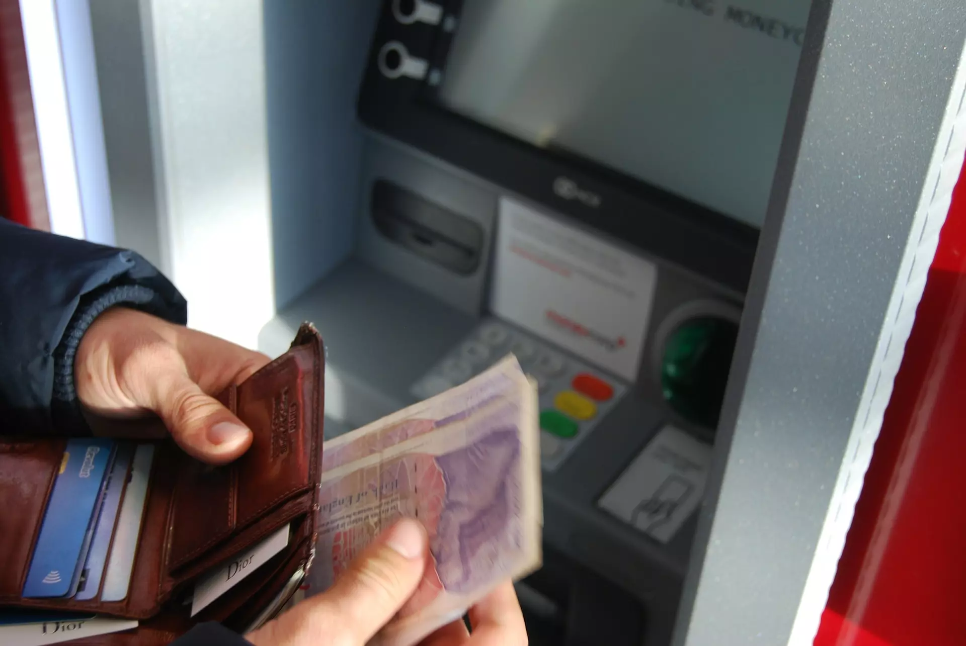 Hands placing banknotes inside a wallet in front of a cash machine